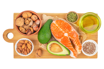 Top view of healthy fats food sources including raw salmon steak, avocado, nuts, seeds and olive oil arranged on wooden cutting board, balanced nutrition and clean eating concept