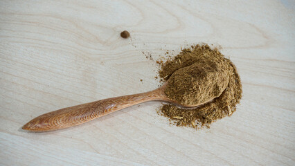 Powdered aquatic animal feed ingredient placed on a wooden spoon over a light natural wood background, representing raw materials used in fish and shrimp feed production
