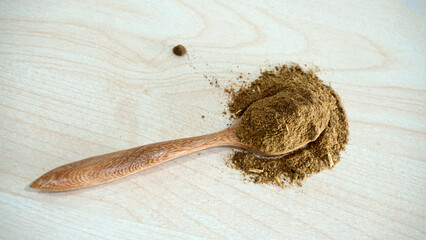 Powdered aquatic animal feed ingredient placed on a wooden spoon over a light natural wood background, representing raw materials used in fish and shrimp feed production
