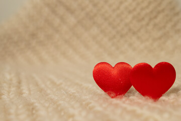 Fototapeta premium A close-up presents two red heart shapes. They sit side by side on a soft, fluffy, white blanket creating a simple Valentine's Day scene. Warm, gentle light fills the frame.