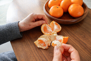 Hands of a senior woman eating a mandarin orange at a wooden table