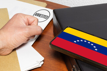 Clenched fist on paperwork with “arrested” stamp next to Venezuelan flag on mobile screen as a...