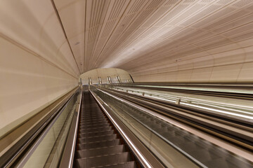 Long architectural perspective down multiple modern escalators and parallel moving walkways in a...