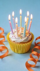 birthday cupcake with lit candles and sprinkles on blue background with orange ribbon streamers, festive party dessert, celebration concept with copy space