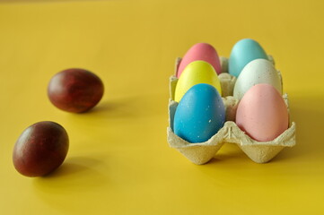 Colorful Easter eggs in cardboard box against yellow background
