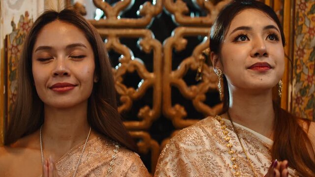 Two beautiful thai women praying in a temple