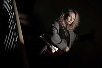 A stylish woman in a coat sits on the stairs. Noir style