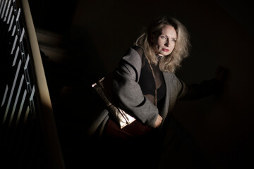 A stylish woman in a coat sits on the stairs. Noir style