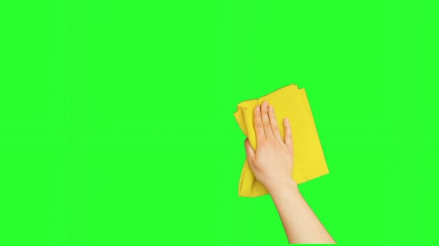 A close-up of a hand using a yellow microfiber cloth to wipe a surface, isolated on a green screen. Keywords: wiping, cleaning, hand, yellow cloth, microfiber, hygiene, household, chore, surface, sani