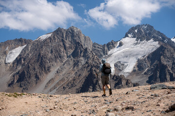 Active hiker with backpack and trekking poles walking on a mountain trail. Freedom and adventure concept in the high mountains.