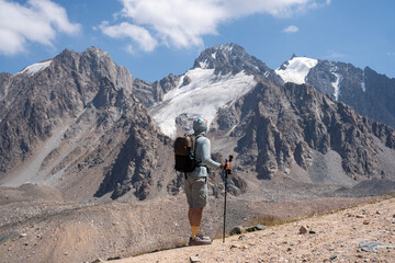 Active hiker with backpack and trekking poles walking on a mountain trail. Freedom and adventure concept in the high mountains.