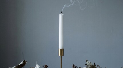 Slender white taper candle extinguished in brass holder with wisps of smoke rising gently.
