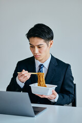 カップ焼きそばを食べながら仕事をする20代の若い男性