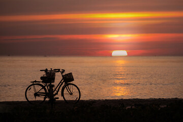 Fototapeta premium Image of the sun setting over the sea. Silhouette of a bicycle parked by the sea against the backdrop of a bright evening sky before dusk.