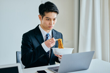 カップ焼きそばを食べながら仕事をする20代の若い男性