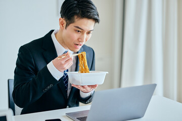 カップ焼きそばを食べながら仕事をする20代の若い男性