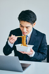 カップ焼きそばを食べながら仕事をする20代の若い男性