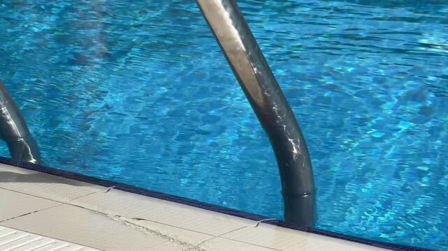 Aluminum ladder descends elegantly into crystal-clear hotel pool water. Modern poolside design blends function with resort luxury vibe.