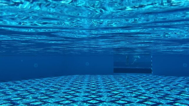 Underwater camera captures mesmerizing sunlight patterns in the pool, with rays creating shimmering caustics and ripples dancing across the tiled bottom.