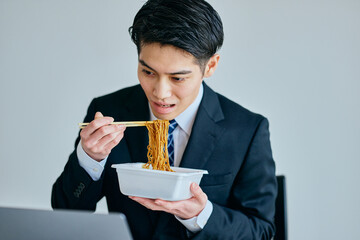 カップ焼きそばを食べながら仕事をする20代の若い男性