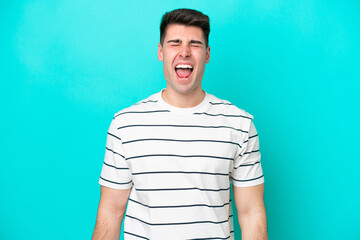 Young caucasian man isolated on blue background shouting to the front with mouth wide open