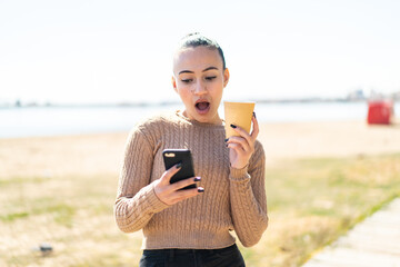 Young moroccan girl  at outdoors using mobile phone and holding a coffee with surprised expression