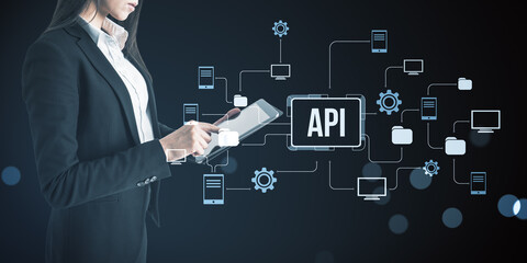 Businesswoman using digital tablet with API network interface and connected devices representing technology and data exchange concept on dark background.