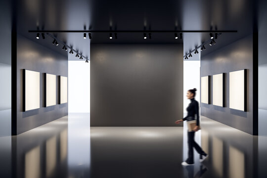 Contemporary art gallery with blank canvases and a woman walking through a modern interior space with dark walls and spotlight ceiling lights.