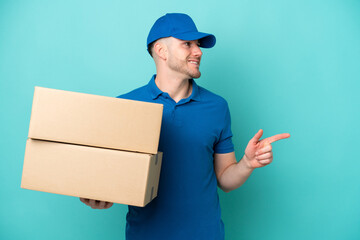 Delivery caucasian man isolated on blue background pointing finger to the side and presenting a product