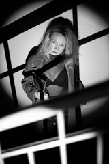 A stylish woman in a coat stands on the stairs. Black and white noir style.