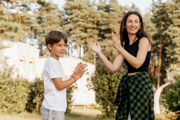 Naklejka premium Happy mother and son playing together outdoors in summer park, enjoying bonding time, smiling and clapping hands, authentic candid family moment in natural light 