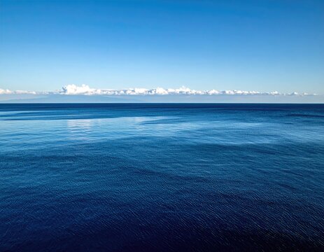 Vast, deep blue ocean under a bright, clear sky with wispy clouds