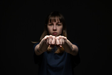 A young woman extends both closed fists toward the camera in a strong, defiant pose, with shallow...