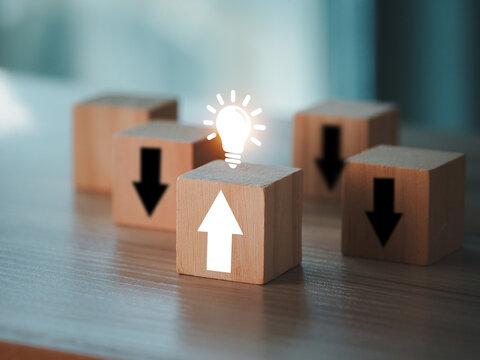 Wooden block with upward arrow and glowing lightbulb symbolizing innovation and leadership among blocks with downward arrows, conceptual business idea and growth inspiration