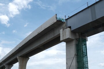Modern elevated bridge under construction with concrete pillars and steel beams, viewed from below against blue sky, showing infrastructure development.
