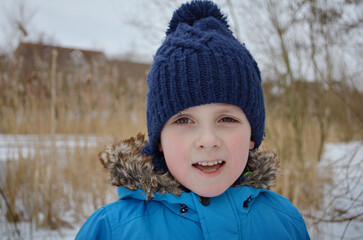 Child boy smiling in winter coat with snowy background near river.