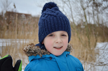 Child boy smiling in winter coat with snowy background near river.
