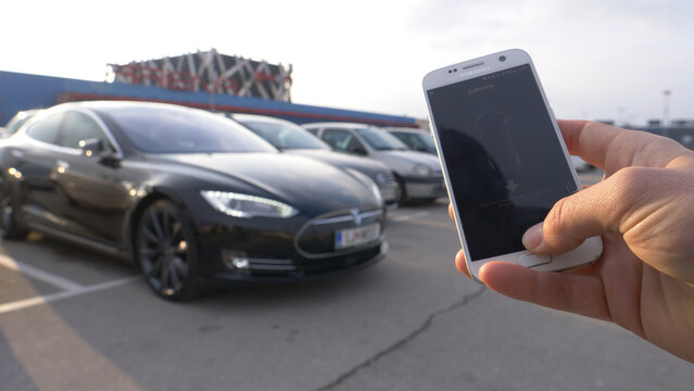 CLOSE UP: Person holding a smartphone parks the remote controlled Tesla car.