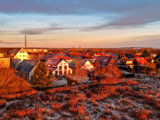 quiet village basks in the golden light of sunrise or sunset, with frosty rooftops and warm tones casting a cozy, peaceful winter atmosphere over the landscape