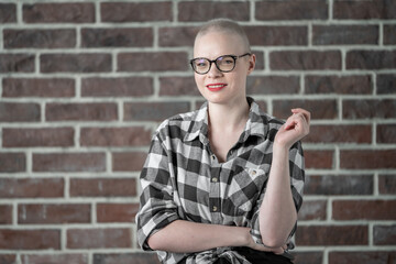 Portrait of a beautiful young caucasian woman with shaved head. Female cancer survivor. Smiling Woman with Glasses Posing Confidently in a Studio Environment. Model Has Glaucoma. Waering Plaid Shirt