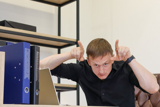 Man at workstation mimicking devil horns with hands