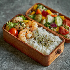 Two Japanese wooden bento boxes filled with grilled shrimp, white rice, and colorful vegetable salad