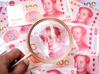 Close-up of Chinese 100 yuan banknotes with gold magnifying glass highlighting Mao Zedong’s...