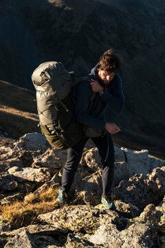 Adventurous hiker stabilizing load on rugged alpine outcrop