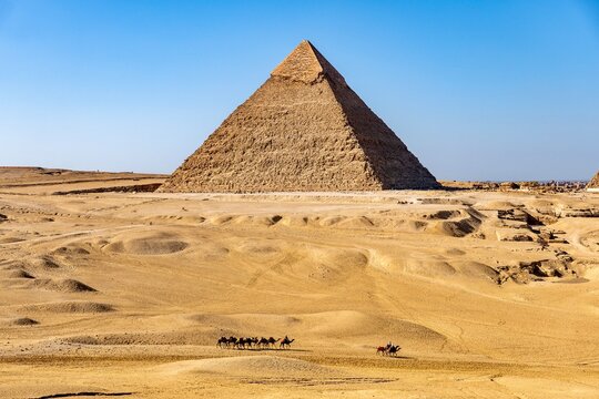 Camel caravan crossing the Egyptian desert with the Pyramid of Khafre at Giza in evening light