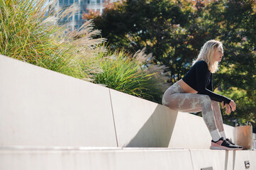 Woman in athletic wear sitting on concrete steps in a park with trees and buildings in the background