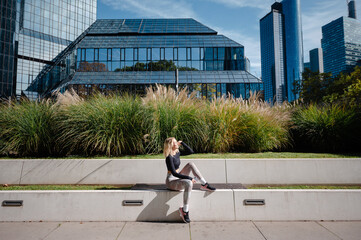 Woman in athletic wear relaxing on a bench with modern architecture and urban greenery