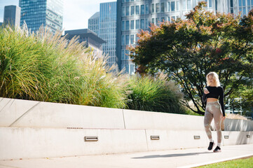 Woman in athletic wear walking outdoors with phone in hand, city buildings in background