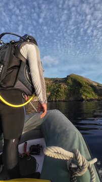 Divemaster seated in inflatable boat holding gear with an island ridge visible in background, Broken Ridge, Indonesia