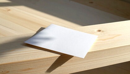A blank white card rests on a wooden surface, casting a soft shadow from the sunlight